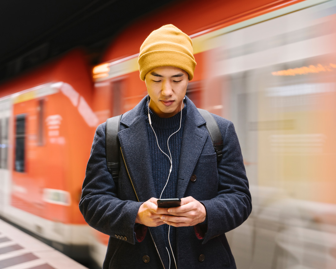 Un uomo con berretto e giacca viene visto usare il suo telefono davanti a un treno.