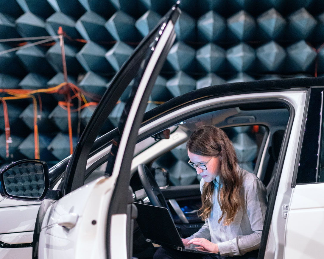 Una donna al posto di guida di un&#039;auto, concentrata sul suo computer portatile.