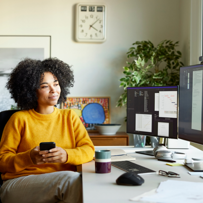 Una donna concentrata sul lavoro, seduta a una scrivania con un computer e un cellulare vicino, in un'efficiente attività multitasking.