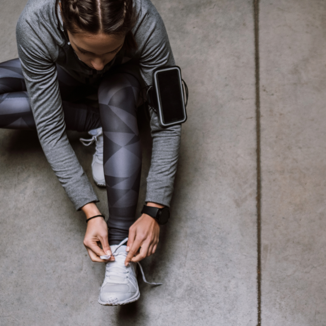 Una donna che si allaccia le scarpe su un pavimento di cemento, preparandosi alle sue attività quotidiane con concentrazione e determinazione.