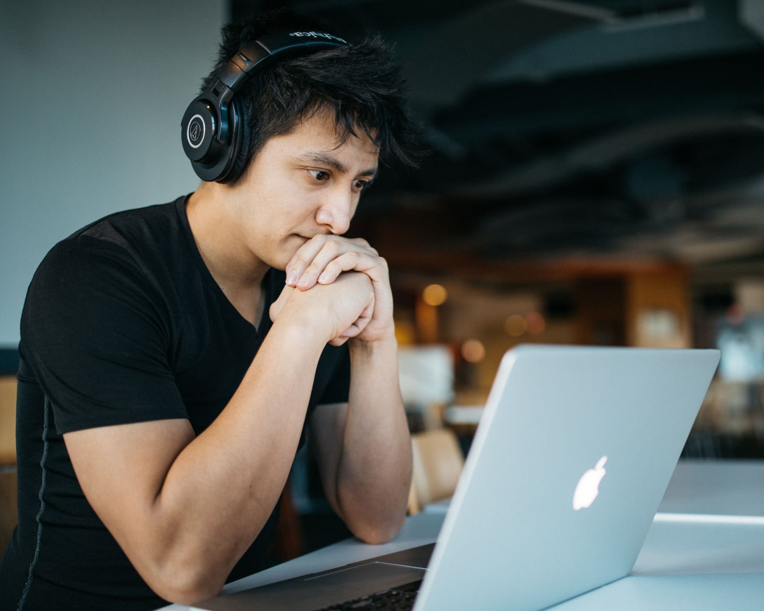 Un uomo impegnato nel lavoro, con le cuffie, è seduto a un tavolo con il suo computer portatile, concentrato e immerso nei suoi compiti.